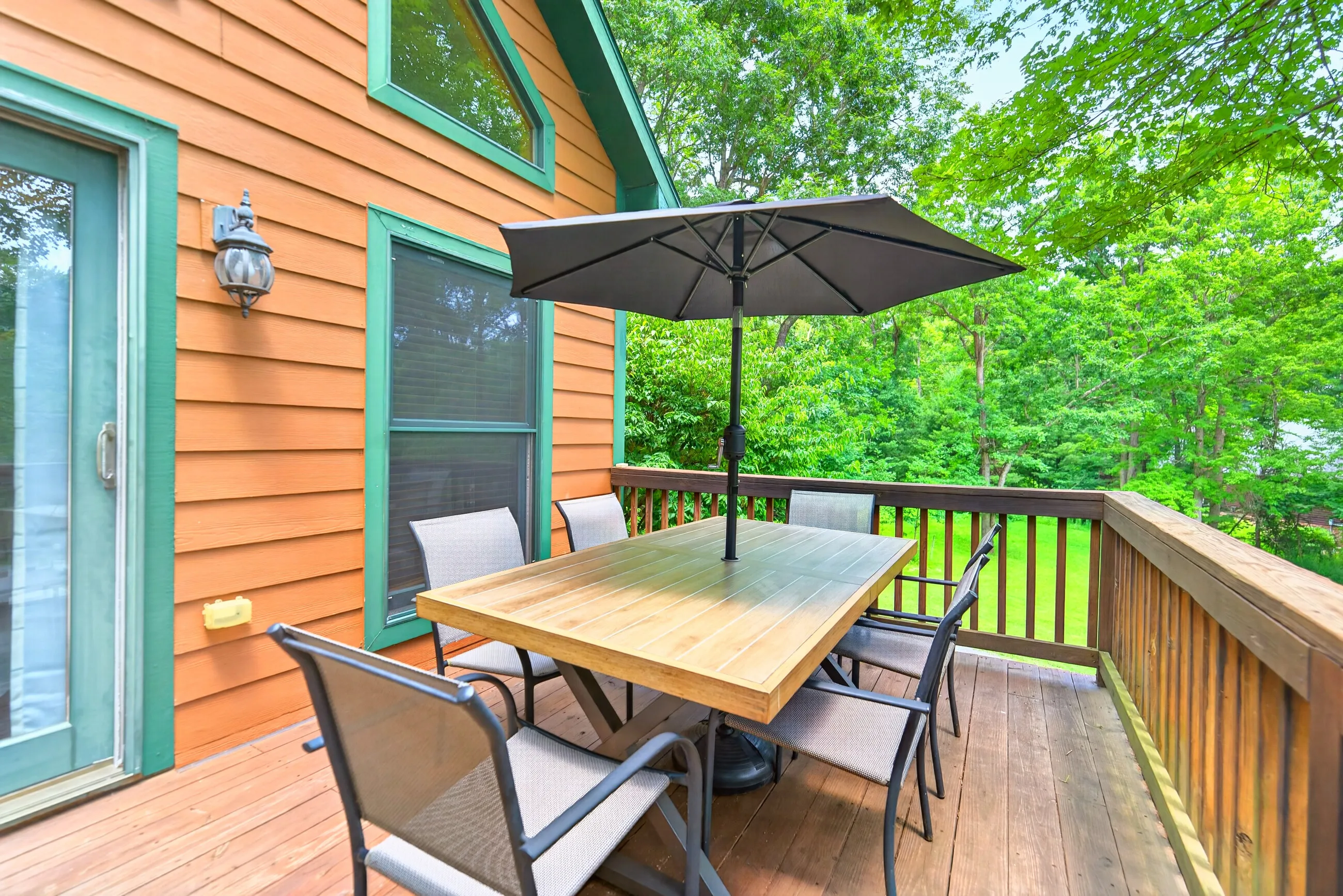 Deck dining table under an umbrella with the woods behind