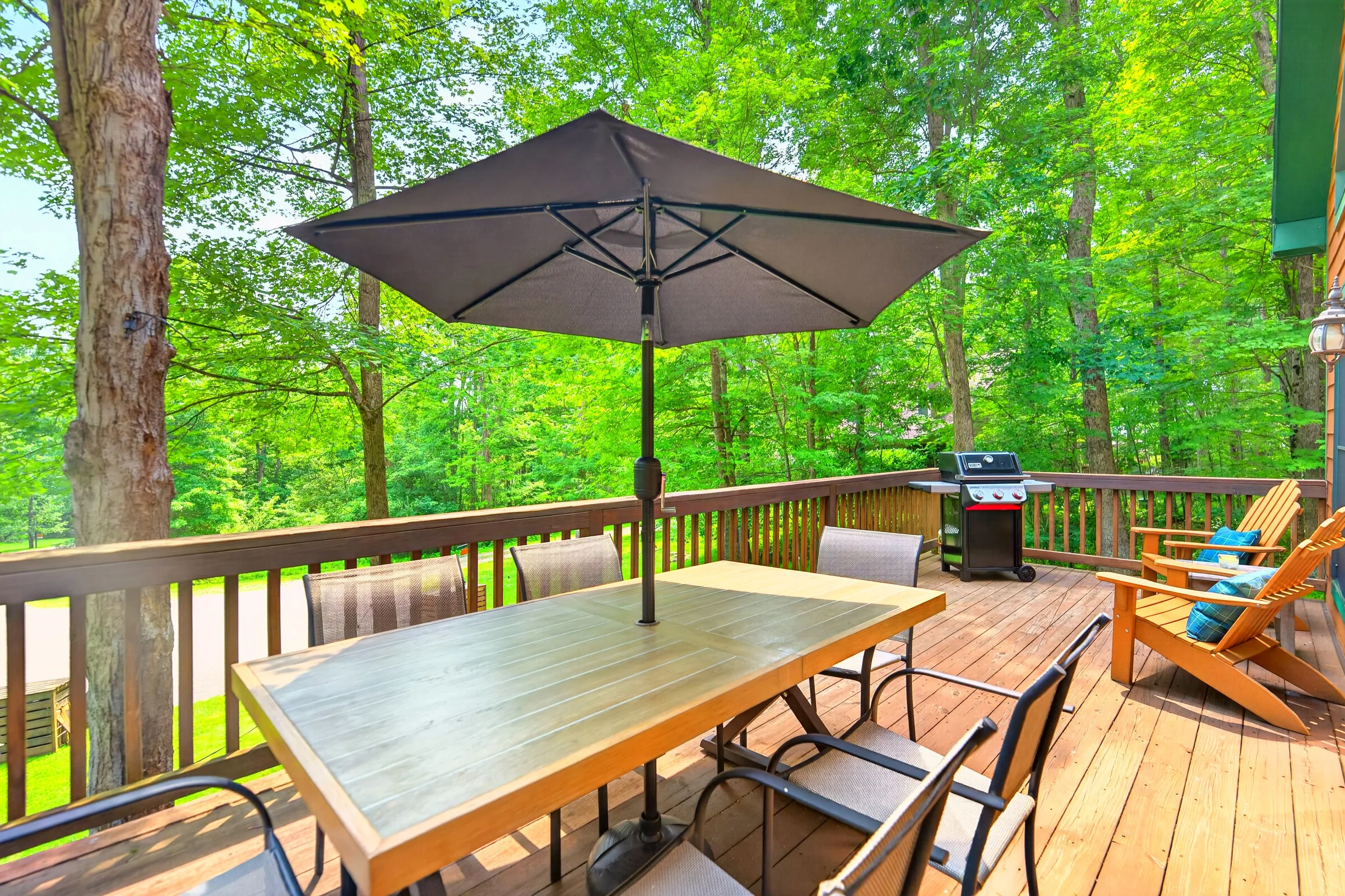 The deck with the grill and the dining table under its umbrella