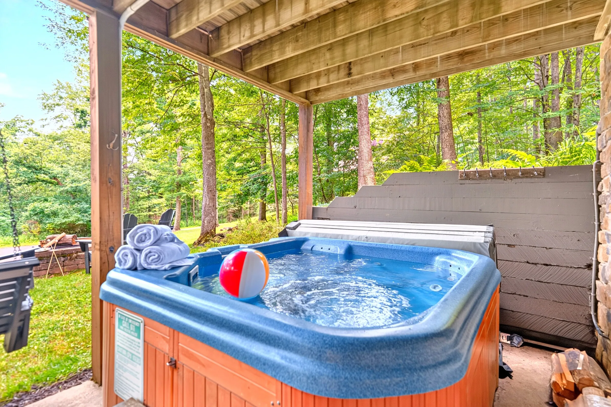 The hot tub under the deck with the woods behind it