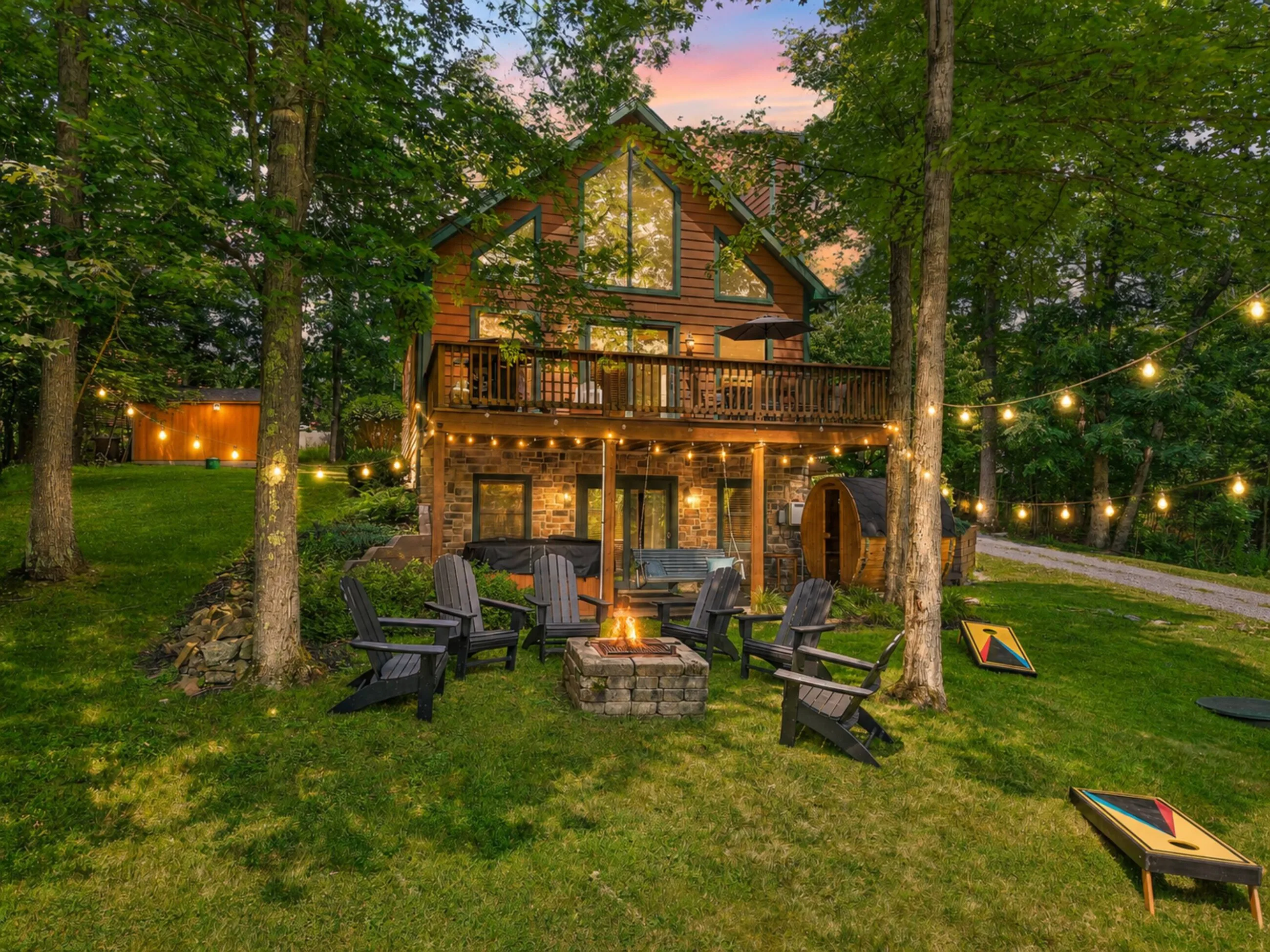 The house lit from inside at twilight, fire pit and string lights on the lawn